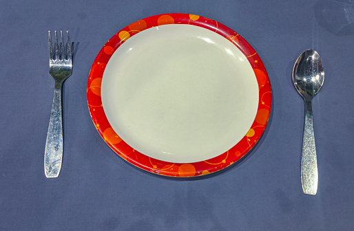 Fork spoon with  empty  plate crockery and red round with blue background in hotel