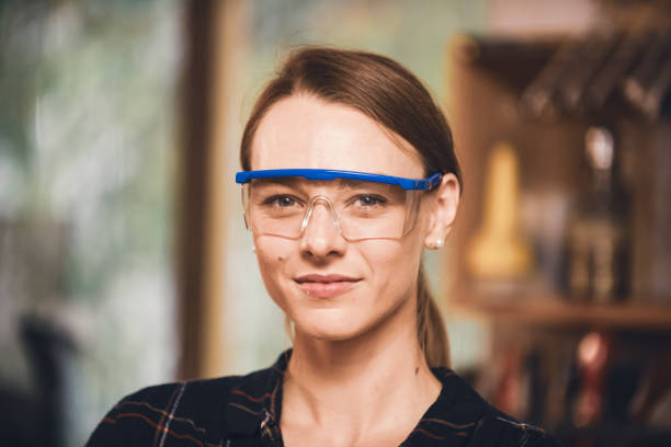 Waist-up portrait of a smiling fit female carpenter with folded arms smiling at the camera.Close up of an attractive female woodworker wearing protective eyewear .