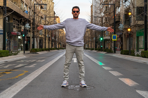 young man in a sweatshirt and glasses in the middle of Gran Via street in Granada, with open arms.