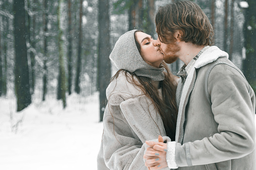 Love romantic young couple. Guy hugging kissing girl in snowy winter forest. Walking,having fun in trees, laughing. Stylish clothes,fur coat,jacket,woolen shawl. Snow lovestory. Romantic date,weekend.