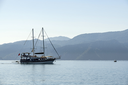 A sailing tourboat at sea in Fethiye, Turkey and mountains with coastline in the background.