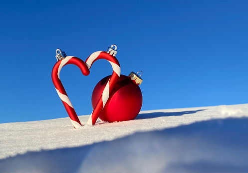 Heart shaped Christmas decoration. Candy canes and Christmas ball in the snow.
