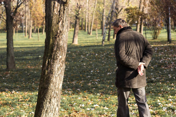 Thai senior man leaning at tree in park