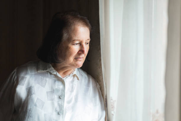 istock Elderly woman standing and looking through the window 1443957491