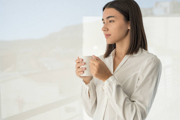 istock Girl standing thinking by window drinking coffee 1443958134