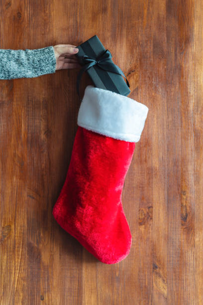istock Woman's hand puts a black gift with a bow in red Christmas stocking. Packaging and preparation of gifts for the celebration. 1443964675