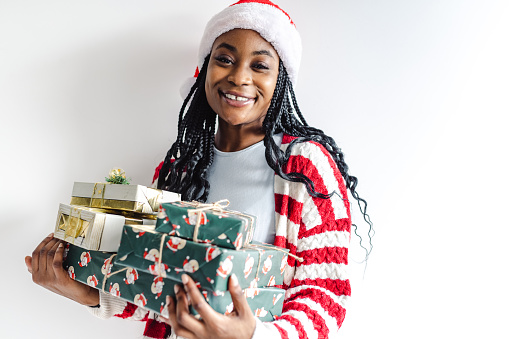 Cheerful woman holding Christmas gifts in front of the white wall