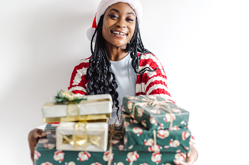 Cheerful woman holding Christmas gifts in front of the white wall and looking at the camera