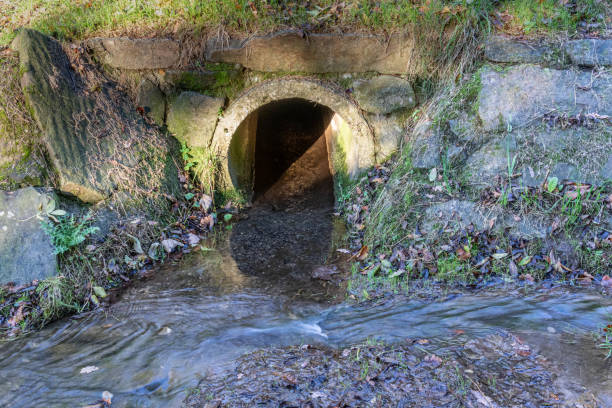 Clean transparent water flowing from concrete drainage pipe into a stream stock photo
