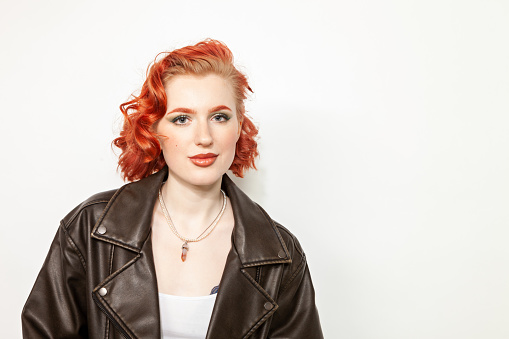 Studio portrait of a young red-haired white woman in a black leather jacket on a white background