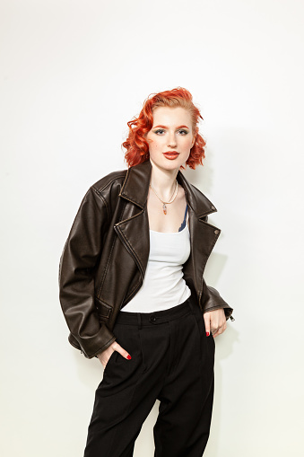 Studio portrait of a young red-haired white woman in a black leather jacket on a white background