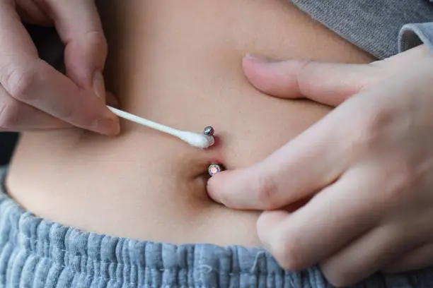 Young girl applying antibiotic cream on her belly button piercing redness infection