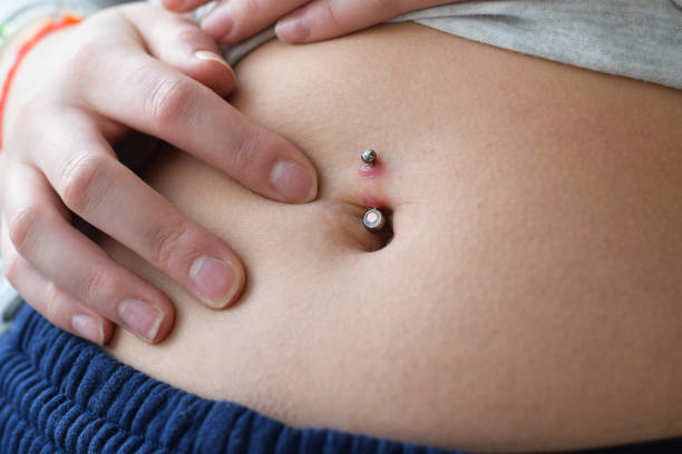 junges mädchen, das ihre bauchnabel-piercing-rötung auf infektion überprüft - piercing stock-fotos und bilder