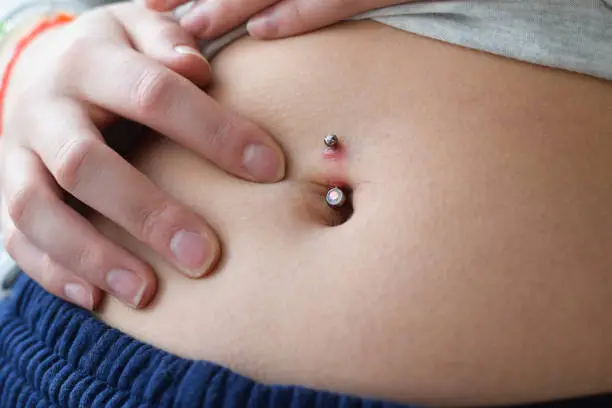 Closeup on young teenage girl stomach checking her belly button piercing redness for infection