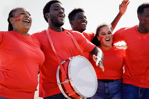 African red sport football fans celebrating team victory in championship game at stadium - Soccer supporters having fun in crowd - Focus on left man face