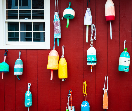 Colorful lobster buoys hang on a red wall in Maine.