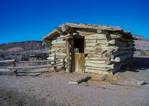 An old deserted wooden cabin with a corral sits empty in the arid desert of Utah