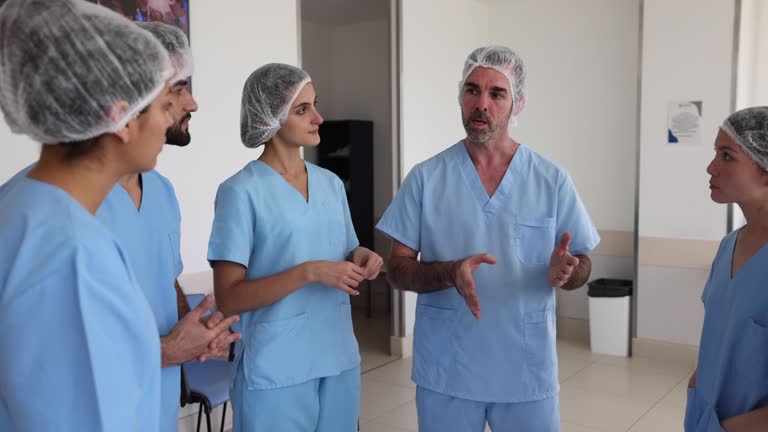 Diverse team of surgeons in a brief meeting outside the OR very focused listening to male doctor