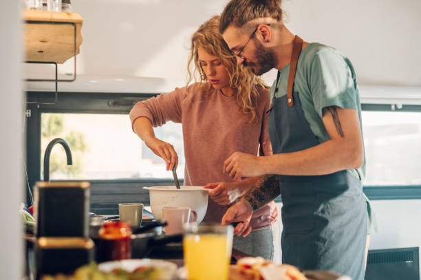 pareja joven preparando el desayuno juntos en la cocina de casa - cooking men caucasian togetherness fotografías e imágenes de stock