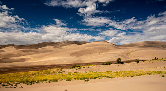 The large area of sand dunes is constantly changing. The park contains some of the largest sand dunes in North America. The bright blue sky with clouds formations create shadows and shades of color like waves.