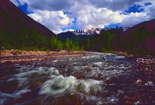 La Platte River spring run off forming small rapids over the rock bed. La Platte Mountains. The cumulus clouds are dramatic as they hang on top of the peaks.