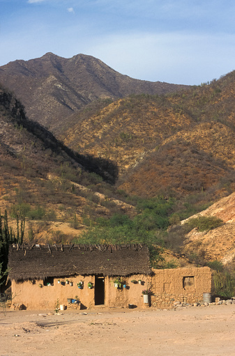 A adobe building sits alone at the bottom of a canyon in Mexico surrounded by rocky peaks