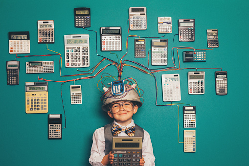 A young boy dressed as a nerd has a unique intelligence with numbers. He is a mathematics and numbers whiz, ready to solve any complex number problem. He is wearing a makeshift helmet and invention which uses many calculators to compute his solutions.