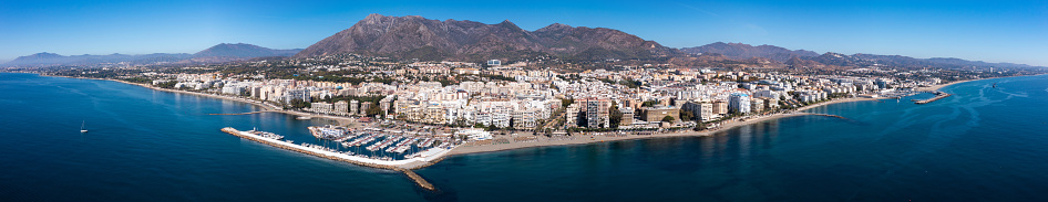 Scenic panoramic view of Spanish coastal city of Marbella by Mediterranean sea in foothills of Sierra Blanca mountain range overlooking harbour with moored pleasure yachts on sunny autumn day