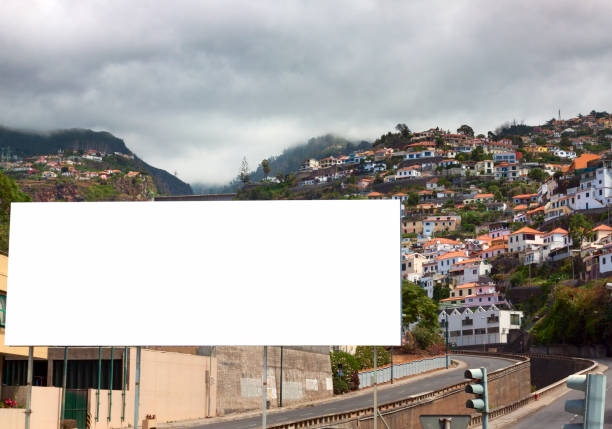 Blank billboard in Funchal, Madeira. Cloudy sky, houses and other dwellings on the hillside in the background, roads in the near foreground.