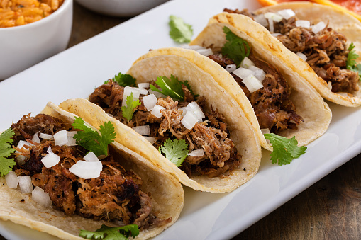 Pork carnitas tacos on corn tortillas served with rice and beans