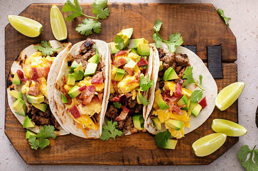 Breakfast tacos with sausage, scrambled eggs, crumbled bacon and diced avocado, overhead shot