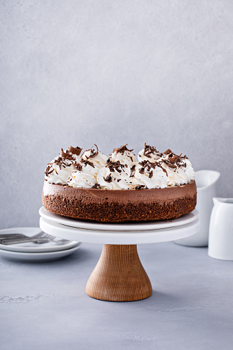 Chocolate cheesecake on a cake stand with whipped cream and chocolate curls