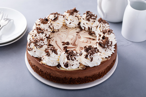 Chocolate cheesecake on a cake stand with whipped cream and chocolate curls