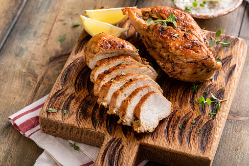 Roasted or seared chicken breast sliced on a cutting board with herbs and spices