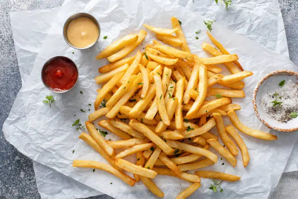 French fries with ketchup and cocktail sauce on a parchment paper