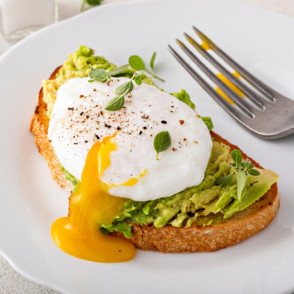 Avocado toast with a perfect poached egg on top with salt and pepper served with coffee for breakfast with runny yolk