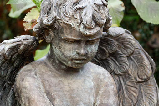 small putto with angel wings on a grave looks sadly to the ground