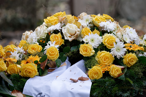 funeral flowers with yellow roses and white mourning bow on a grave with fallen autumn leaves