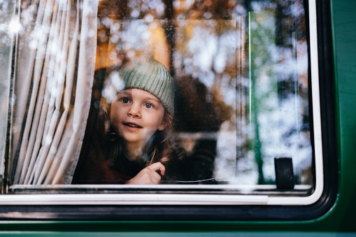 Happy young girl sitting in a van and looking outside while camping in nature.