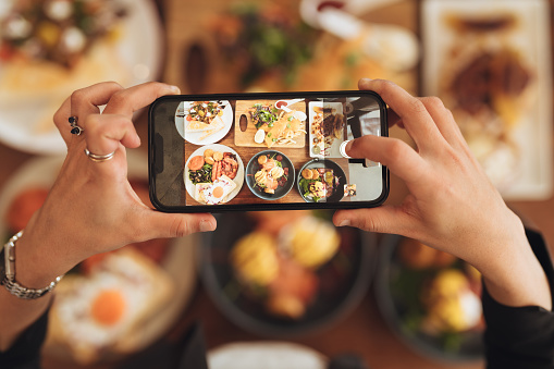 Human hand holding phone taking photo of food.