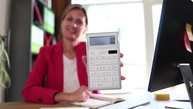 Smiling female accountant shows number one hundred on calculator