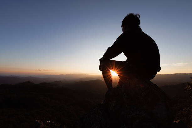 silhouette eines jungen mannes, der auf dem berg bei sonnenuntergang zu gott betet. frau hebt die hände in anbetung. konzept der christlichen religion. - god freedom arms raised high angle view stock-fotos und bilder