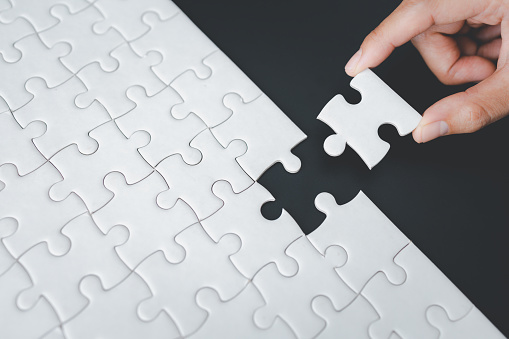 Woman assembling a jigsaw puzzle she is adding the last missing piece, solutions and challenges concept,  Hand put the last piece of jigsaw puzzle to complete the mission