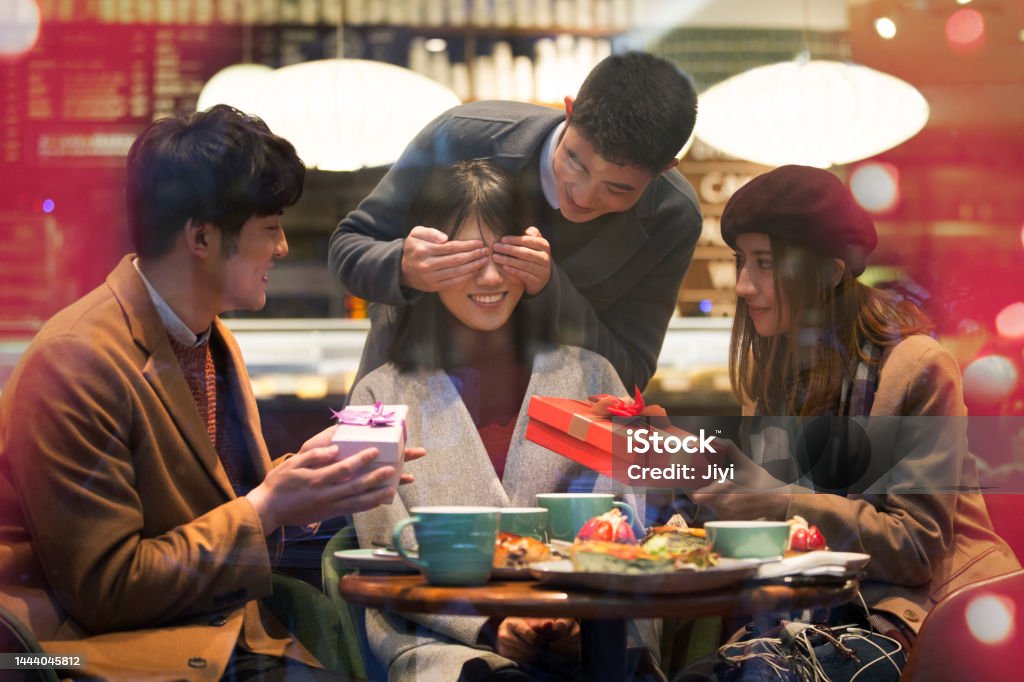 Young East Asians sitting in a restaurant giving surprise gifts to friends in winter - stock photo Suitable for shopping, young people, commercial street, commercial square, fashion, consumption, business, weekend, entertainment, dating, festival, shopping district, afternoon tea, urban life, urban leisure, catering industry, fashion industry, gift, mobile payment, contactless payment, overspending, print advertising Birthday Stock Photo