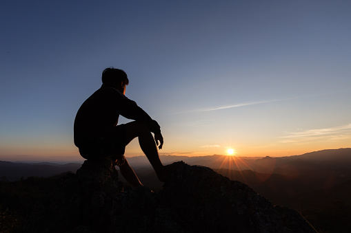 silhouette of Sad man sitting alone on top of a mountain at sunset, Depression and loneliness.  The concept of stress and gloom.
