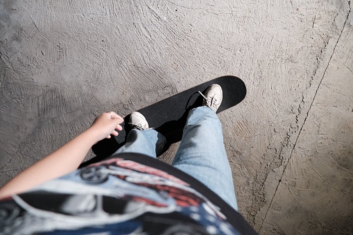 A POV of a skater in baggy jeans and cool graphic T-shirt skateboarding on a concrete floor