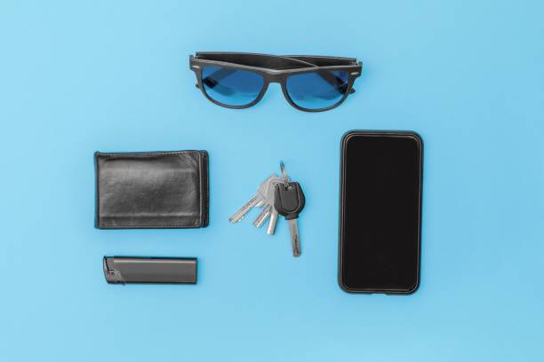 Modern man items, on table cell phone sunglasses lighter wallet keys in black on blue background Top view of modern man items, on table cell phone sunglasses lighter wallet keys in black on blue background phone wallet keys stock pictures, royalty-free photos & images