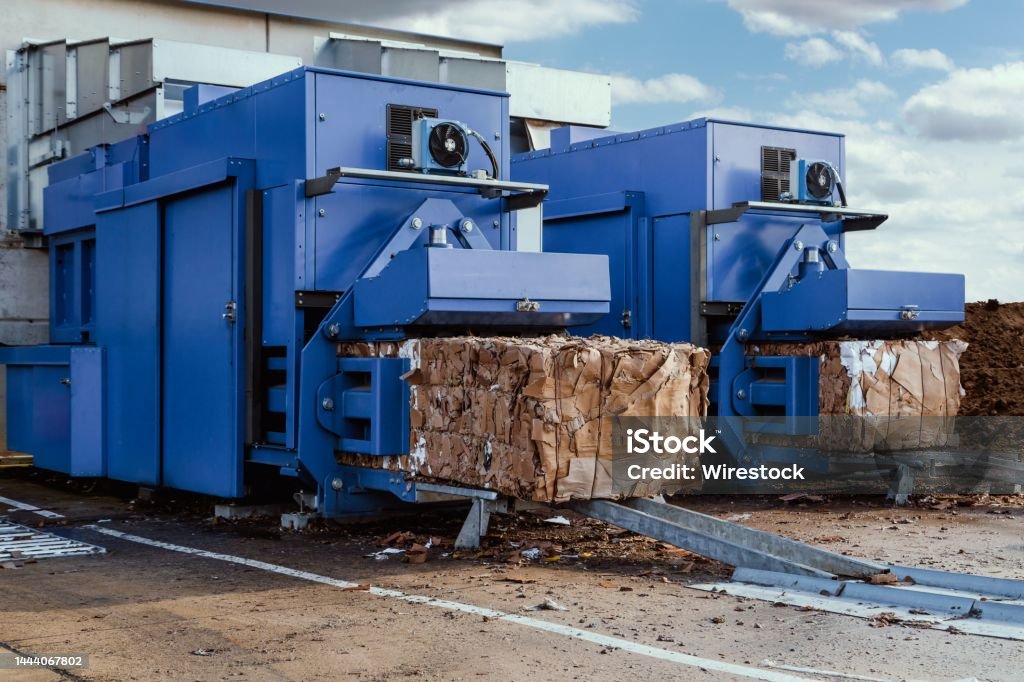 Paper squeezer container and a garbage press machine recycle cardboard into reusable material bales A blue paper squeezer container and a garbage press machine recycle cardboard into reusable material bales Bale Stock Photo