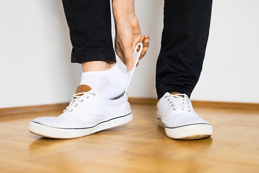 A closeup of a person putting on white sneakers with shoehorn