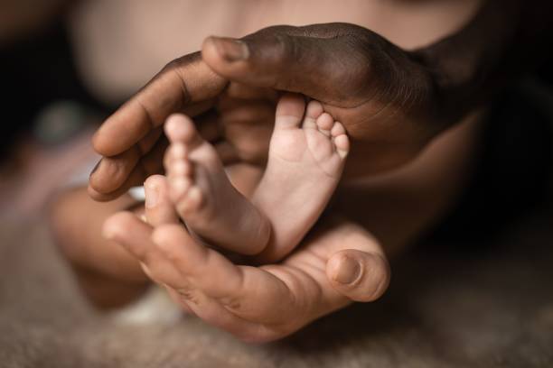 hermosa vista de la familia interracial sosteniendo pies de bebé en las manos, mezclado por el color de la piel blanco y negro - newborn baby human foot photography fotografías e imágenes de stock